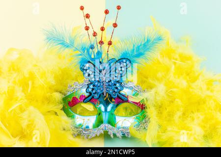 Vorderansicht Mardi Gras türkisfarbene Maske mit gelbem und grünem Hintergrund. Farbenfrohes blaues Kostümzubehör mit Federn für Party und venezianischen Karneval. Stockfoto
