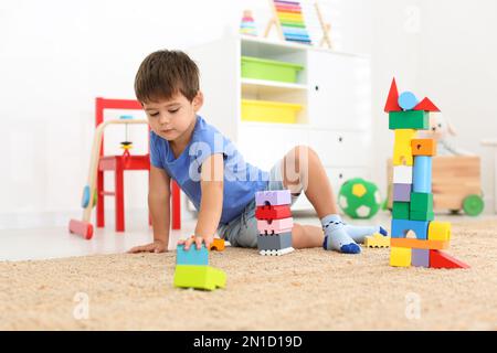 Süßer kleiner Junge, der zu Hause mit bunten Bausteinen auf dem Boden spielt. Pädagogisches Spielzeug Stockfoto