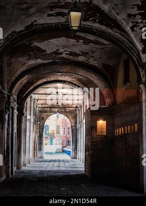 Blick durch einen bogenförmigen Gang auf den Straßen von Venedig zu einem Kanal. Stockfoto