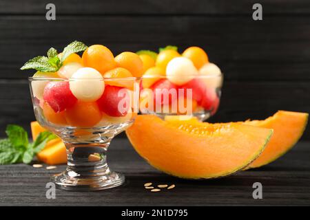 Melonen- und Wassermelonenbällchen mit Minze in der Dessertschüssel auf einem schwarzen Holztisch Stockfoto