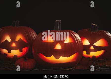 Leuchtender Jack O'Laternen auf dem Tisch in Dunkelheit. Halloween-Dekor Stockfoto