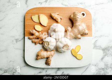 Ingwer und frischer Knoblauch auf weißem Marmortisch, Draufsicht. Natürliche Heilmittel gegen Kälte Stockfoto