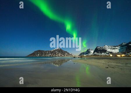 Nordlichter (Aurora Borealis) über schneebedeckten Bergen mit Blick auf Skagsanden Beach, Ramberg, Nordland County, Lofoten Islands, Norwegen Stockfoto