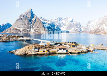 Blick aus der Vogelperspektive auf den Berggipfel Olstind und das türkisfarbene Meer rund um das Dorf Sakrisoy und die reine Bucht, die Lofoten-Inseln, Norwegen, Skandinavien und Europa Stockfoto