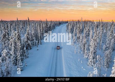 Dramatischer Himmel bei Sonnenaufgang über einem Auto, das in den verschneiten Wald fährt, Luftaufnahme, Kangos, Norrbotten County, Lappland, Schweden, Skandinavien, Europa Stockfoto