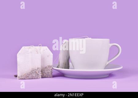 Teetasse mit Kräuterteebeuteln auf violettem Hintergrund Stockfoto