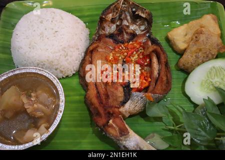Gebratener Fisch mit Sambal, Gemüse aus Indonesien mit weißem Reis, isoliert auf Bananenblatt Stockfoto