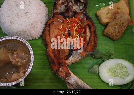 Gebratener Fisch mit Sambal, Gemüse aus Indonesien mit weißem Reis, isoliert auf Bananenblatt Stockfoto