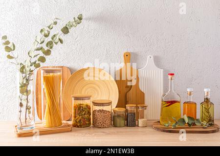 Ein Set aus verschiedenen gefüllten Gefäßen zur Lagerung von Schüttgütern und Glasflaschen mit verschiedenen Arten von organischem Öl auf dem Hintergrund von Schneidebrettern Stockfoto