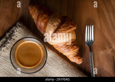 Croissant mit Espresso in weißer Tasse auf Holztisch Stockfoto