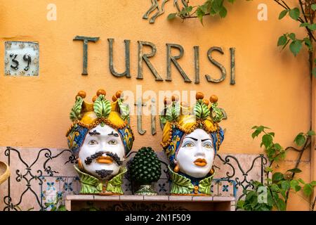 Taormina, Sizilien, Italien: Farbenfrohe, traditionelle, große Keramik-Blumentöpfe mit bemalten Gesichtern an orangefarbenen Wänden außerhalb von Turrisi Stockfoto