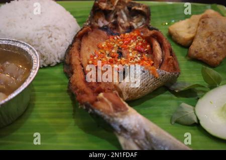 Gebratener Fisch mit Sambal, Gemüse aus Indonesien mit weißem Reis, isoliert auf Bananenblatt Stockfoto