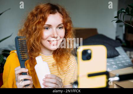 Rothaarige Bloggerin sendet Live-Bewertungen von Schönheitsprodukten für Haare Stockfoto