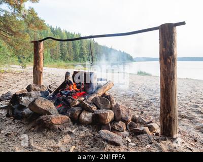 Kochen im Topf über Feuer. Touristisches Camp am Sandstrand des Sees Kenozero. Camping und Wandern in Karelien, Russland. Stockfoto