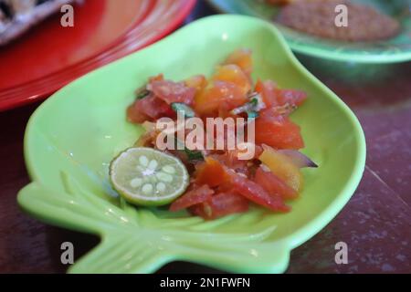 Tomate Sambal oder scharfe Tomate Sambal mit Zutaten, Schalotten, roten Chilis, Knoblauch und Salz. Serviert mit gegrilltem Fisch. Stockfoto