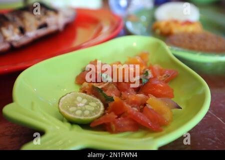 Tomate Sambal oder scharfe Tomate Sambal mit Zutaten, Schalotten, roten Chilis, Knoblauch und Salz. Serviert mit gegrilltem Fisch. Stockfoto