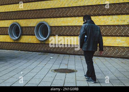 Mann in schwarzer Lederjacke auf dem Bürgersteig Stockfoto