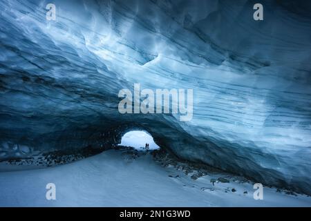 Silhouetten von ein paar Wanderer am Eingang einer Eishöhle mit blauen Schattierungen und Texturen in Zermatt Stockfoto