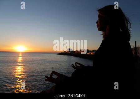 Frau, die Yoga-Meditation am Meer bei Sonnenuntergang als Konzept für Stille und Entspannung praktiziert, Cadiz, Andalusien, Spanien, Europa Stockfoto