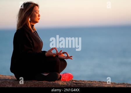 Frau, die vor Sonnenuntergang Yoga-Meditation am Meer praktiziert, als Konzept für Stille und Entspannung, Spanien, Europa Stockfoto