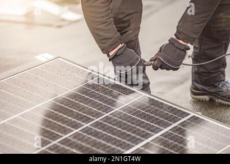 Der Solarpaneelinstallateur verbindet die Module mit einem elektrischen Kabel oder Steckerdraht. Montagearbeiten auf dem Dach, Anschluss von Solarpaneelen an Stockfoto