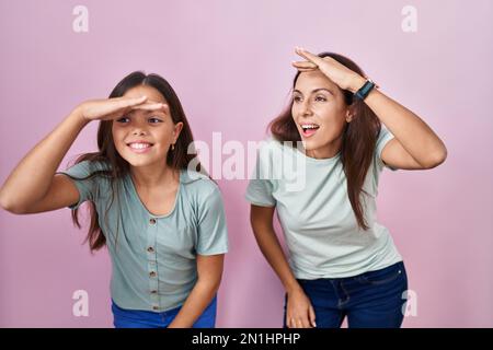 Junge Mutter und Tochter, die über rosa Hintergrund standen, waren sehr glücklich und lächelten weit weg mit Hand über Kopf. Suchbegriff. Stockfoto