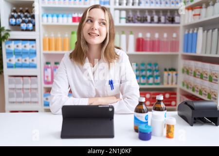 Junge weiße Frau, die in einer Apotheke arbeitet, die Tabletten benutzt, die von der Seite blickt, mit einem Lächeln auf dem Gesicht, natürlichem Ausdruck. Selbstbewusst lachen. Stockfoto