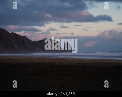 Idyllischer schwarzer Sand Te Henga Bethells Beach mit Felsformationen im Hintergrund während des Sonnenuntergangs auf West Auckland North Island Neuseeland Stockfoto