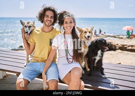 Mann und Frau Paar lächeln selbstbewusst und umarmen sich am Meer mit Hunden Stockfoto