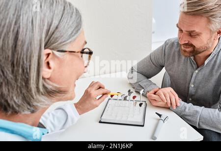 Audiologin bietet BTE-Hörgeräte für Männer mit Hörproblemen zur Behandlung seiner Taubheit an. Hörgeräteauswahl Stockfoto