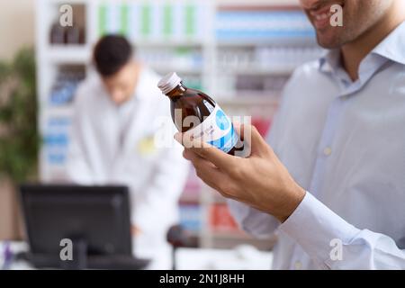Zwei hispanische Männer, Apotheker und Klient, die in der Apotheke per Computer Medikamentenetiketten lesen Stockfoto
