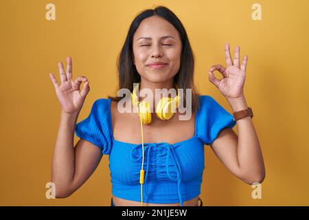 Hispanische junge Frau, die auf gelbem Hintergrund steht, entspannt und mit geschlossenen Augen lächelt und Meditationsgeste mit den Fingern macht. Yoga-Konzept. Stockfoto