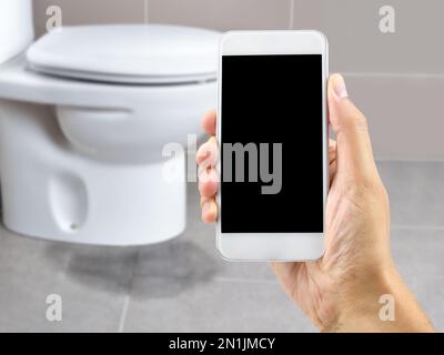 Eine Hand, die ein Smartphone hält, um den Profi anzurufen, um ein Wasserleck in der Toilette zu reparieren Stockfoto