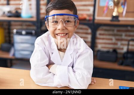 Ein süßer spanischer Schüler, der sich auf den Tisch lehnt, mit den Armen gekreuzten Gesten im Labor Stockfoto