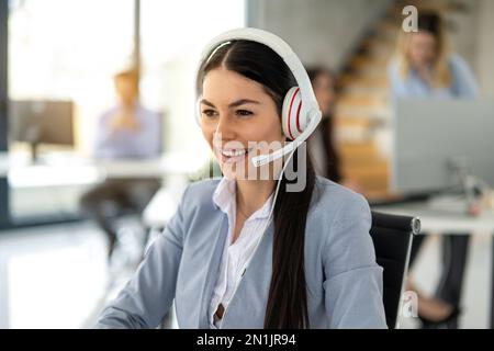 Porträt einer hübschen, weiblichen Online-Agentin, die ein weißes Headset trägt und während eines Telefonats beim Kundendienst mit dem Kunden spricht Stockfoto