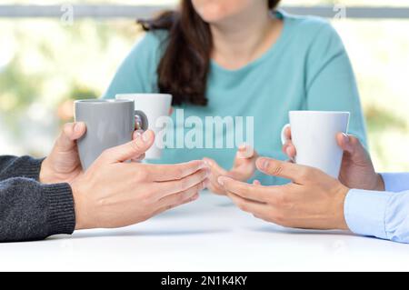 Drei Freunde unterhalten sich und halten Kaffeetassen Stockfoto