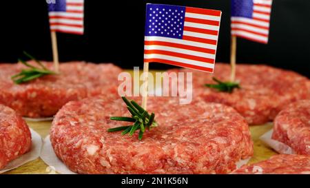 Runde, frische, rohe Hackfleisch-Burger mit amerikanischer Flagge und Rosmarin-Zweigen. Nahrungsmittel für den Unabhängigkeitstag in der Hausküche. Schließen. Stockfoto