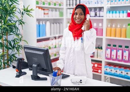 Eine junge, schöne Apothekerin, die telefoniert, indem sie einen Computer in der Apotheke benutzt Stockfoto