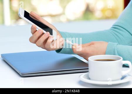 Mädchen Hand Smartphone in einer Tabelle zu Hause mit einem Fenster im Hintergrund Ladegerät anschließen Stockfoto