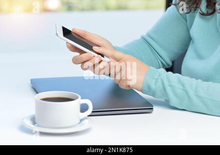 Freigestellte Aufnahme einer Geschäftsfrau, die ein Mobiltelefon und einen Laptop an seinem Schreibtisch benutzt Stockfoto