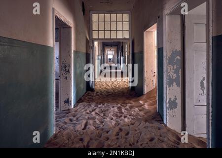 Ein mit Sand gefüllter Korridor im Krankenhaus der Geisterstadt Kolmanskop, Namibia, mit einer gespenstisch bewegungsunscharfen Figur am Ende Verbessern, verarbeitetes Bild. Stockfoto