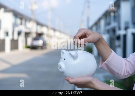 Geld sparen, um ein Haus zu kaufen, Geld in Sparschwein vor Immobilien zu geben. Stockfoto