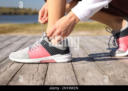 Sportliche Frau, die an einem sonnigen Morgen im Freien Schnürsenkel bindet Stockfoto