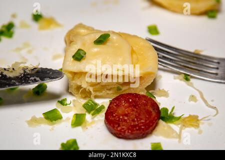 Traditionelles ukrainisches Pierogi auf weißer Platte mit selektivem Fokus. Serviert mit gebratener Wurst und frischem Schnittlauch. Nahaufnahme Stockfoto