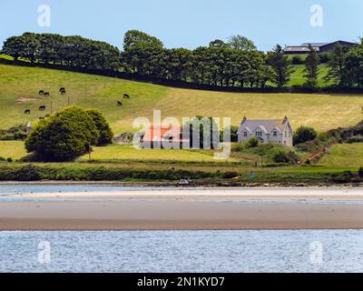 Ein Haus am grünen, hügeligen Ufer der Clonakilty Bay. Ländliche irische Landschaft. Die malerische Natur Irlands im Sommer, Haus in der Nähe von grünen Bäumen und bsb Stockfoto