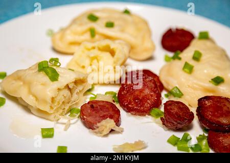 Traditionelles ukrainisches Pierogi auf weißer Platte mit selektivem Fokus. Serviert mit gebratener Wurst und frischem Schnittlauch. Nahaufnahme Stockfoto