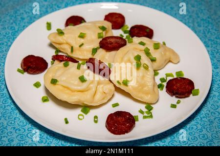 Traditionelles ukrainisches Pierogi auf weißer Platte mit selektivem Fokus. Serviert mit gebratener Wurst und frischem Schnittlauch. Nahaufnahme Stockfoto