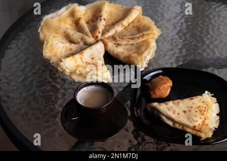 Foto auf einem Glastisch mit Pfannkuchen und abgekochter Kondensmilch und einer Tasse Kaffee aus nächster Nähe Stockfoto