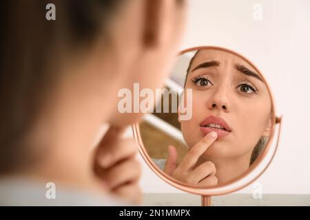 Emotionale Frau mit Herpes berührt Lippen vor dem Spiegel vor hellem Hintergrund Stockfoto