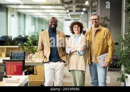 Drei erfolgreiche Manager oder Makler in intelligenter Freizeitkleidung schauen vor die Kamera, während sie mit grünen Pflanzen im Freiraumbüro stehen Stockfoto